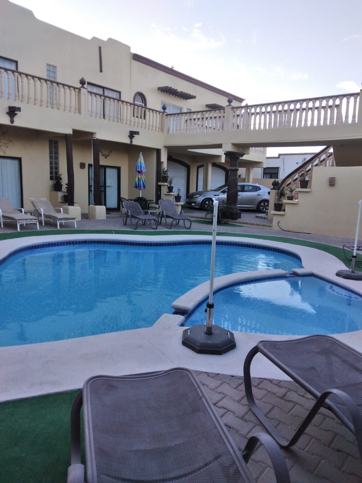 A freeform pool and spa combo with a curved white deck in a warm stucco courtyard with balustraded balconies.