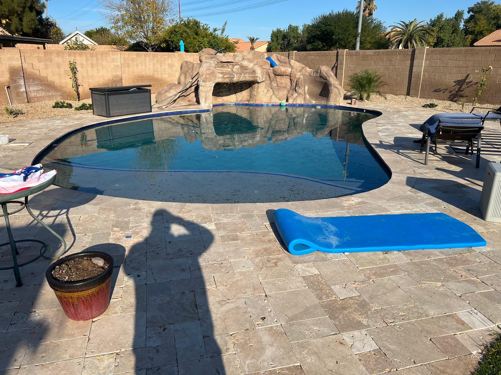 A freeform dark-bottom pool with a sculpted rock grotto and slide, surrounded by travertine pavers and desert planting.