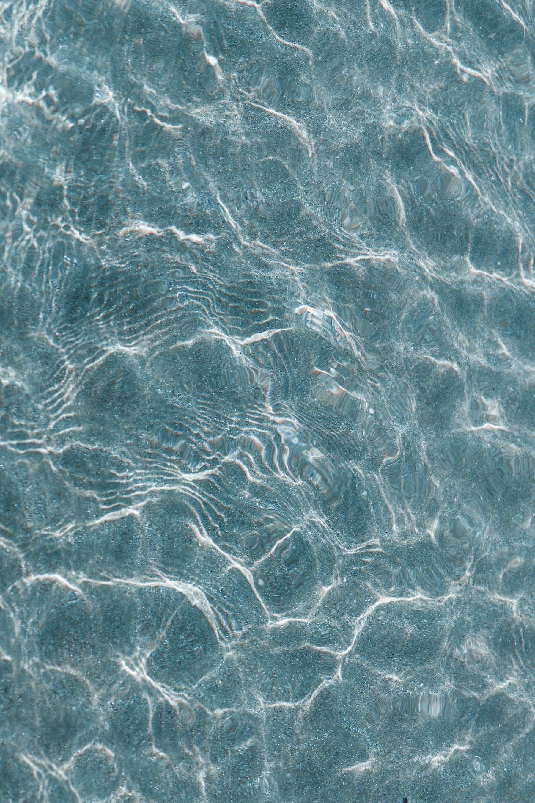 Close-up of sunlit teal pool water rippling over a mottled pebble interior.